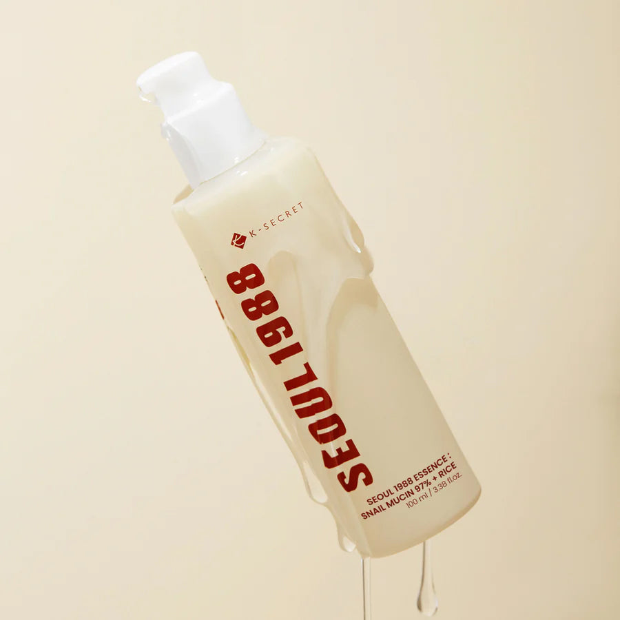 Lys beige flaske med K-Secret Essence: Snail Mucin 97% + Rice 100 ml, dækket af essens mod neutral baggrund.