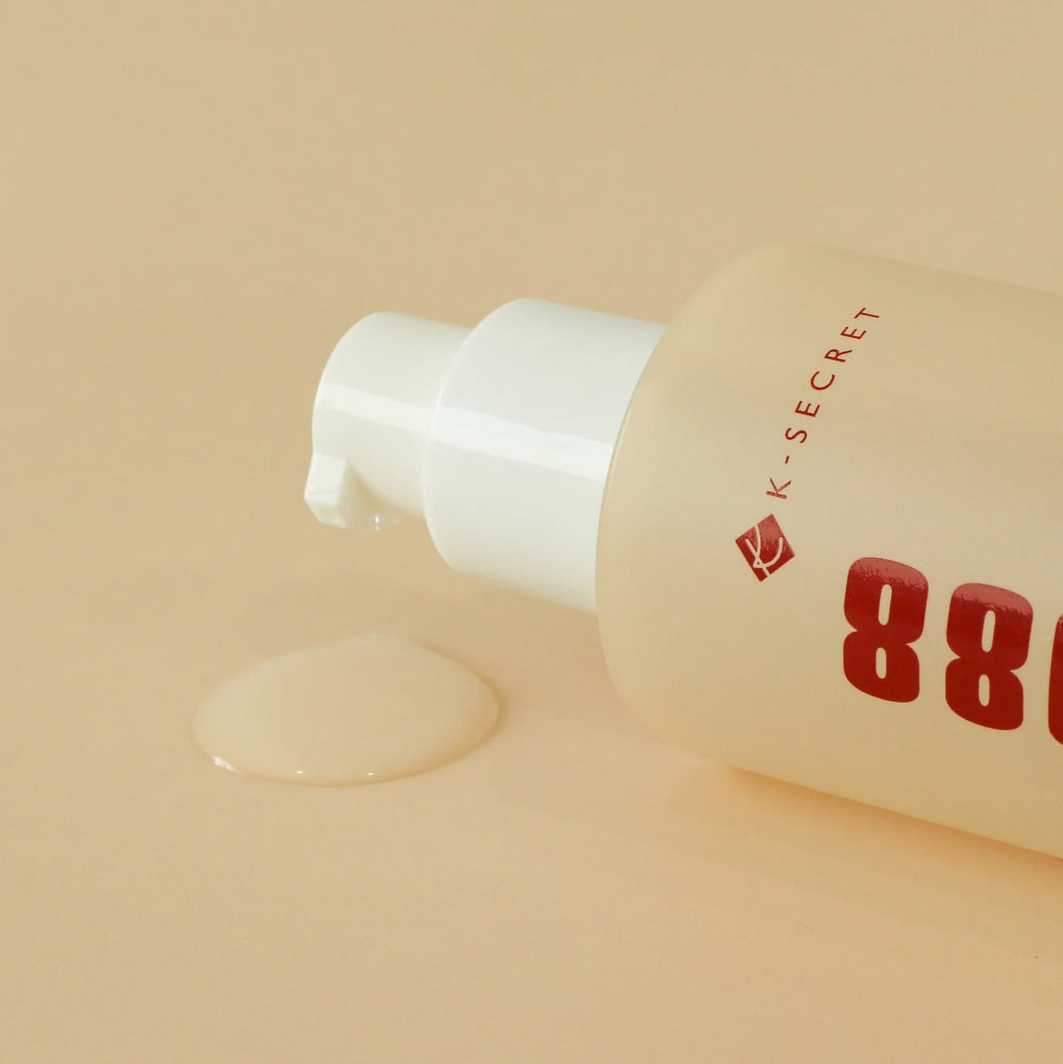 Flaske K-Secret Essence: Snail Mucin 97% + Rice 100 ml med pumpe, essensen spildt på beige overflade.